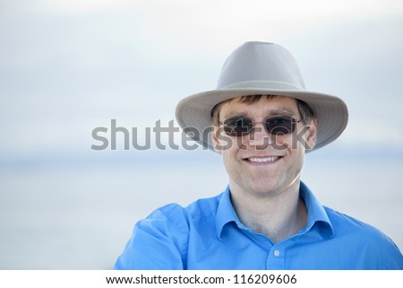 Handsome man wearing hat and sunglasses in early forties with blurred water background