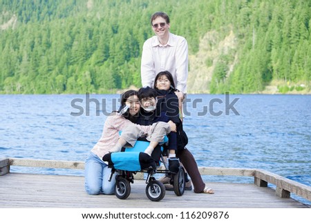 Disabled boy in wheelchair surrounded by family on lake pier