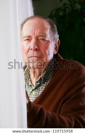 Elderly senior man standing next to window, alone