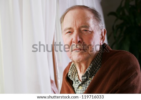 Elderly senior man standing next to window, alone