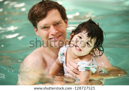Father and toddler boy swimming in pool. Child has cerebral palsy.