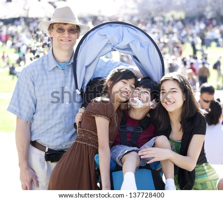 Large multiracial family in crowd with disabled child in wheelchair. Flowering cherry trees in background.