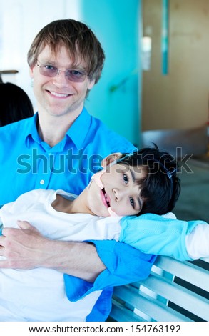 Handsome Caucasian father in forties holding biracial disabled son in arms. Child has cerebral palsy.