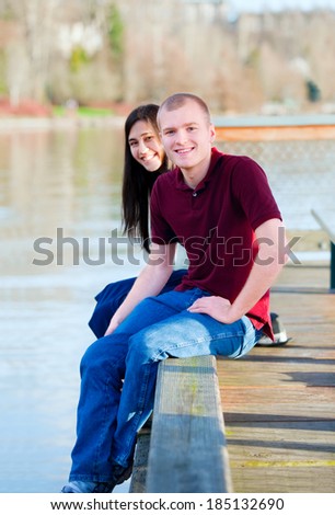 Beautiful young interracial couple sitting on wooden dock over lake, dangling feet over sides