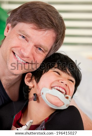 Handsome father holding disabled seven year old son, smiling together