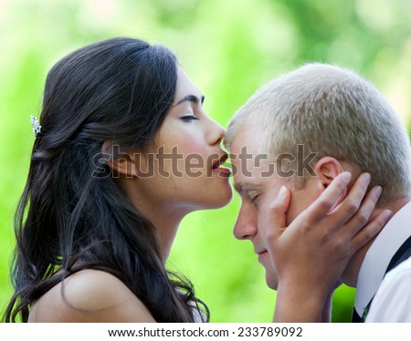 Biracial bride kissing Caucasian groom on forehead. Diverse couple