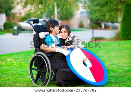 Disabled brother hugging older sister while sitting in wheelchair outdoors