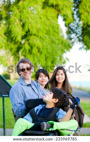 Disabled boy in wheelchair with family outdoors on sunny day sitting at a park