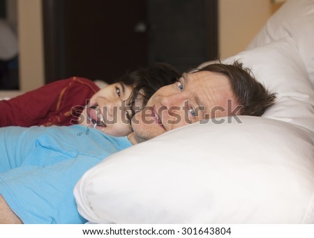 Caucasian father taking a nap with young disabled biracial son, in bed, laughing and talking together. Child has cerebral palsy.