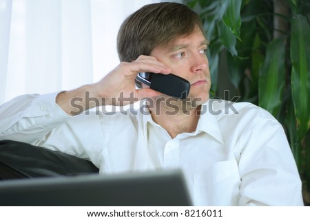 Handsome businessman working on laptop and using cell phone in casual attire.