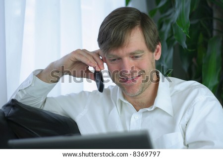 Handsome businessman working on laptop and using cell phone in casual attire.