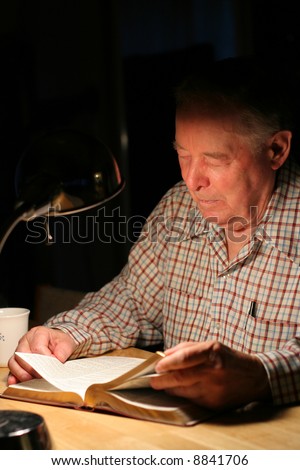 Elderly man reading the Bible by lamplight, dark background shadows