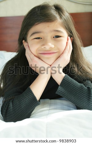 Six year old girl chin on hands thinking while lying down on bed