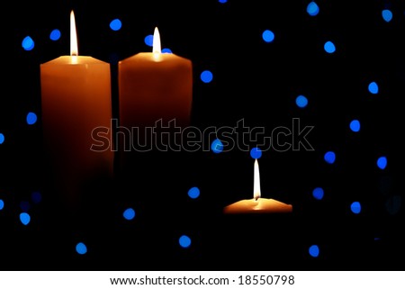 Three burning candles with blue lights in background, dark shadows