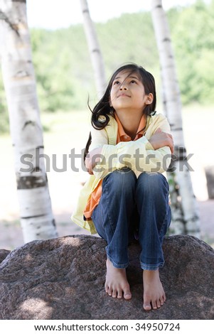 Little girl sitting under trees, looking up