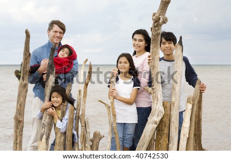 Father with his five children standing by lake shore near driftwood fencing in summer