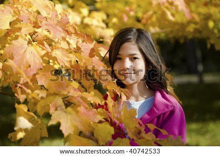 Little biracial asian girl standing amongst bright autumn leaves