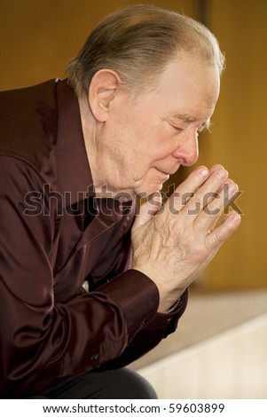 Elderly man praying in dark church