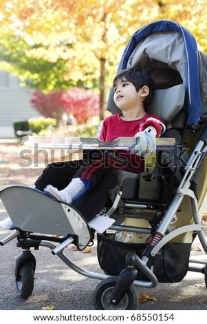 Disabled boy with cerebral palsy in medical stroller enjoying an autumn day outdoors at the park