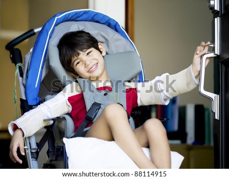 Handsome four year old disabled boy in wheelchair opening front door, smiling a welcome