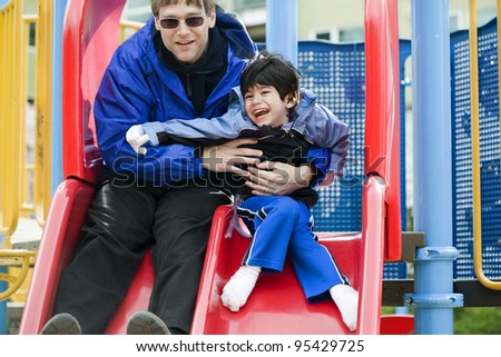 Father going down slide with disabled son who has cerebral palsy