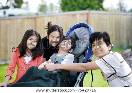 Five year old disabled boy in wheelchair lovingly surrounded by his three older brother and sisters