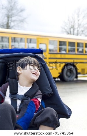 Disabled five year old boy in wheelchair, by school bus