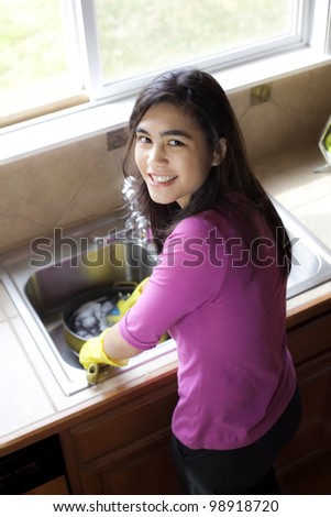 Teen girl happily washing dishes at kitchen sink