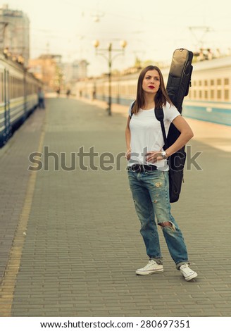 Girl with a guitar at train station. Retro toned image