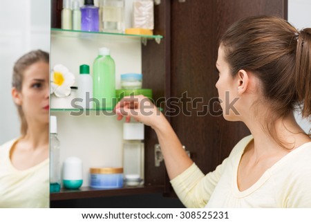 Beautiful girl choosing beauty products from the bathroom cabinet