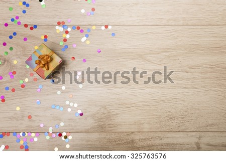 Gift box and colorful confetti on a wooden background