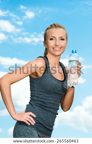 Fitness beautiful blonde woman drinking  water after sports on the background of sky and clouds