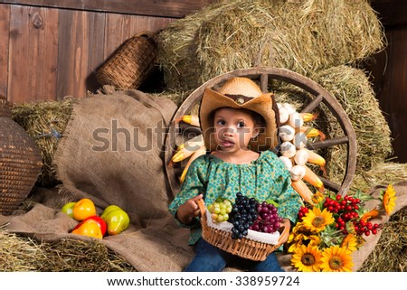 Thoughtful little african girl in cowboy hat sitting in the hay with fruit