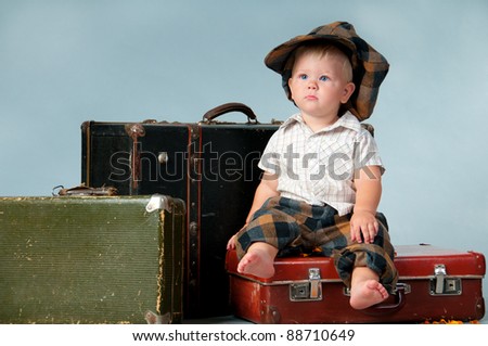 Sad little boy sitting on an old suitcase. He is wearing a hat