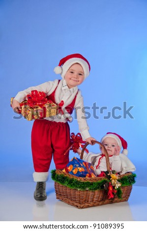 Happy New year. Charming Santa helpers. Little boy and a girl dressed as Santa bring Christmas gifts in a wicker basket.