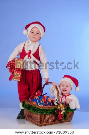 Happy New year. Charming Santa helpers. Little boy and a girl dressed as Santa bring Christmas gifts in a wicker basket.