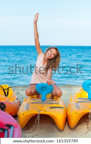 Young woman is sitting on the sea boat with her right hand up smiling
