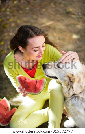 Happy woman eating watermelon with her white dog golden retriever