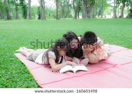 Mother daughter and son reading a book in the garden.