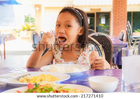 Asian girl eating rice and food on table in restaurant.