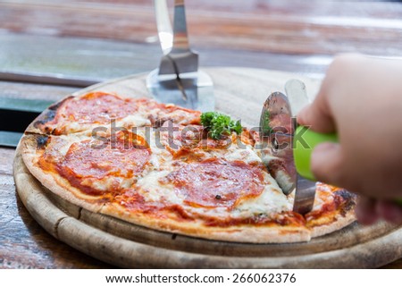 Salami pizza on wood tray and pizza cutter in restaurant.