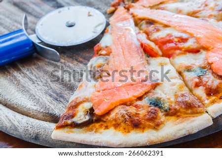 Salmon pizza on wood tray and pizza cutter in restaurant.