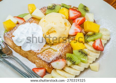 Honey toast with ice cream vanilla, kiwi, mango, banana, apple and strawberry on white plate.