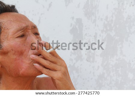 Asian old man smoking cigarette. Face filled with wrinkles.