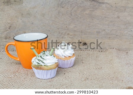 Coffee cup of orange and Cupcake matcha green tea and chocolate put on a hemp cloth on the wood.