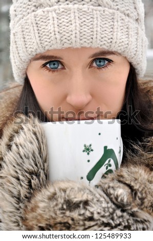 Beautiful, young brunette woman drinking from the winter mug outdoors.