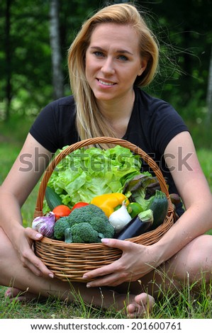 Blond woman sitting holding a basket with vegetables, smiling