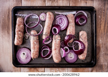 Baking tray with six raw pork and apple sausages covered with red onions