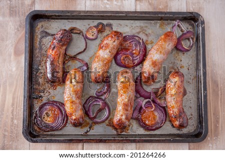 Baking tray with six baked pork and apple sausages covered with red onions and mango chutney. Shallow DoF on middle of image.