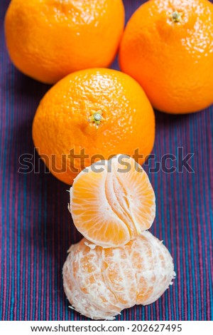 Mandarin orange segments with three whole mandarins in the background on a colorful cloth